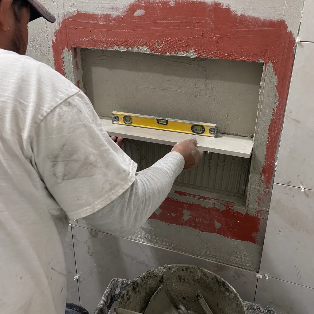 Contractor installing a tiled shower niche shelf using a level